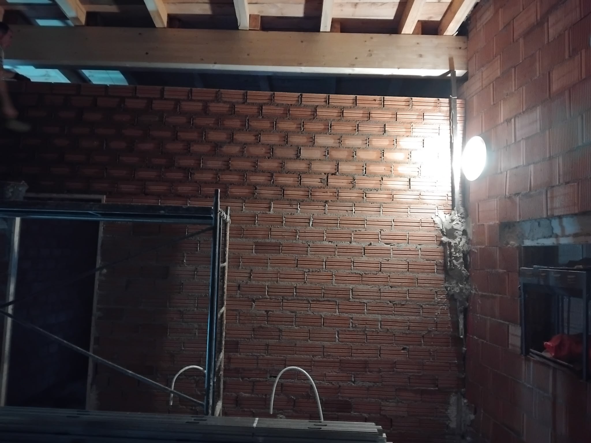 Interior en obra con muro de ladrillo y vigas de madera de cubierta
